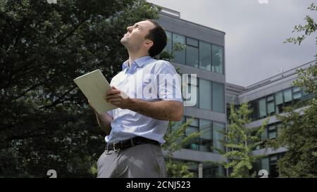 Businessman standing in city park, near office buildings using t Stock Photo