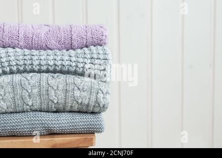 Stack of cozy knitted clothes on a wooden ladder. Scandinavian style. White wooden wall Stock Photo
