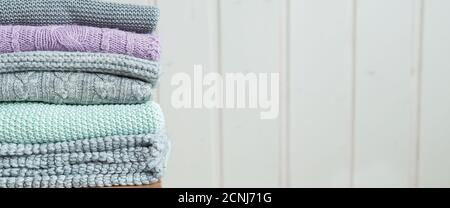 Stack of cozy knitted sweaters on a wooden ladder. Scandinavian style. White wooden wall Stock Photo