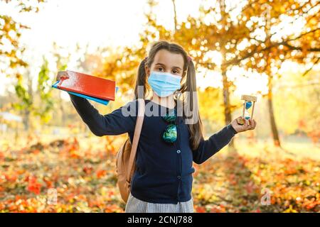 Little girl wearing medical face mask prevent pollution on fallen leaves at park. Stock Photo