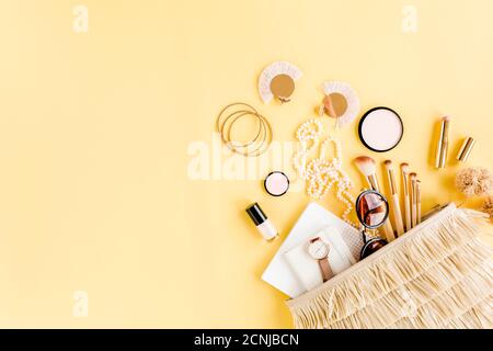 Woman straw bag with travel accessories, makeup brushes, cosmetics, golden accessories on yellow background.  Stock Photo