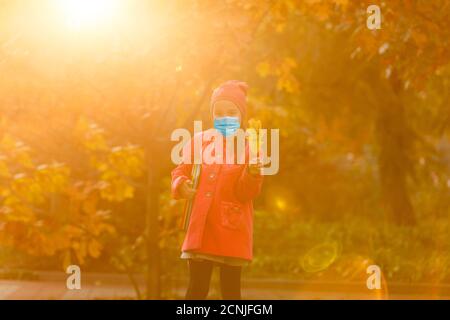 Little girl wearing medical face mask prevent pollution on fallen leaves at park. Stock Photo