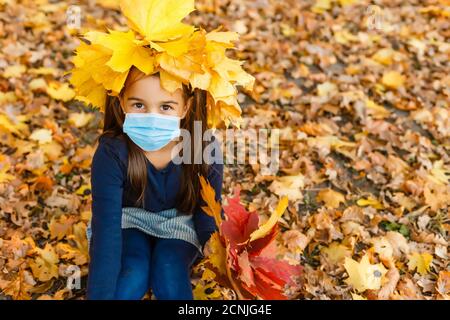 Little girl wearing medical face mask prevent pollution on fallen leaves at park. Stock Photo