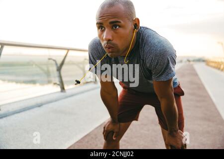 Relaxed african sportsman resting while listening to music with earphones on a bridge Stock Photo