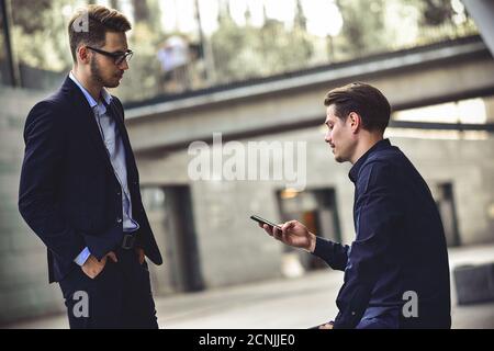 Bad news. Sad and frustrated young caucasian man sit at street and hold a phone. Stock Photo