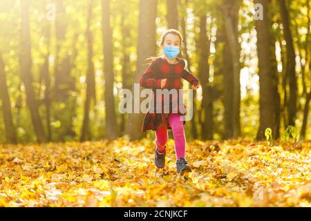 Little girl wearing medical face mask prevent pollution on fallen leaves at park. Stock Photo