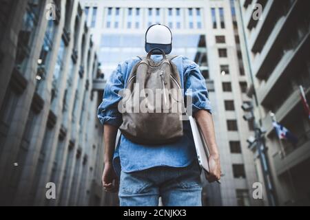 Cheerful young man with backpack enjoying walk the city with laptop and snap back.