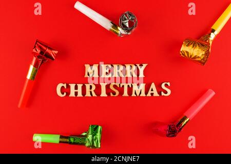 wooden letters on red background. Merry christmas lettering on red paper surrounded party whistles Stock Photo