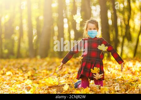 Little girl wearing medical face mask prevent pollution on fallen leaves at park. Stock Photo