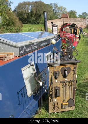 Traditional blacksmith, Brian Greaves, works on board his narrowboat on the Grand Union canal and sells his metalwork from the towpath near Braunston. Stock Photo