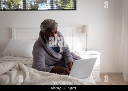 African American senior man lying on a bed in a bedroom, using a laptop, social distancing and self isolation in quarantine lockdown Stock Photo
