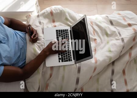 African American senior man lying on a bed in a bedroom, using a laptop, social distancing and self isolation in quarantine lockdown Stock Photo
