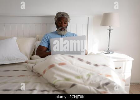 African American senior man lying on a bed in a bedroom, using a laptop and smiling, social distancing and self isolation in quarantine lockdown Stock Photo