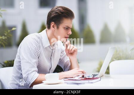 Attractive businessman using a laptop and smiling while working in cafe. Stock Photo