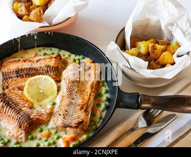 Salmon fillet with creamy peas and carrots served with roasted potatoes in a rustic pan Stock Photo