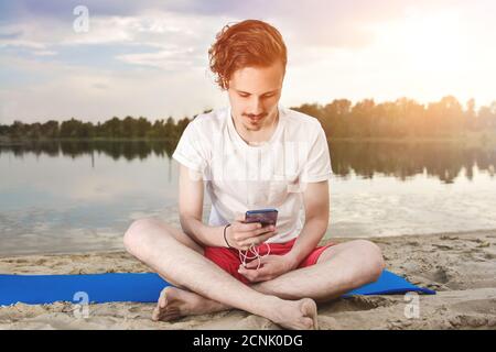 Man is sitting on the beach at lake and writing a sms on phone. Stock Photo