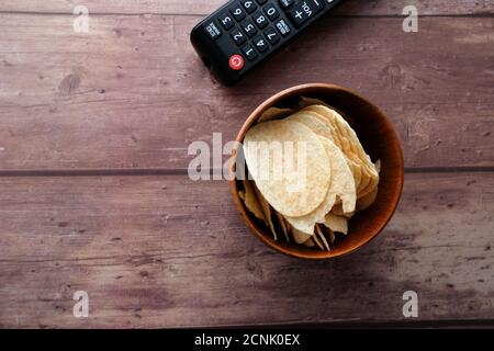 bowl of chips and tv remote on wooden background . Stock Photo