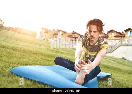 Man performing yoga young fitness man outdoor doing exercise. leg stretch Stock Photo