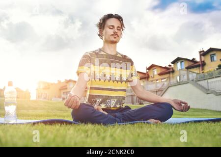 Young man meditating outdoors in the park, sitting with eyes closed and his hands together.enjoying nature, yoga and meditation Stock Photo