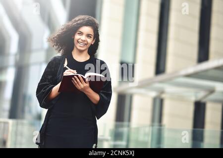 Portrait of a smiling mixed race woman making notes in a notepad while standing outdoors. Stock Photo