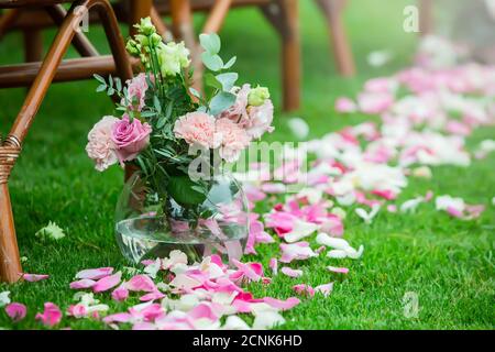 Outdoor wedding ceremony decoration setup. Path with petals, chairs decorated with colorful ribbons, white arch. Stock Photo