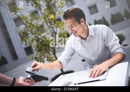 Handsome man is giving a credit card in city cafe. Stock Photo