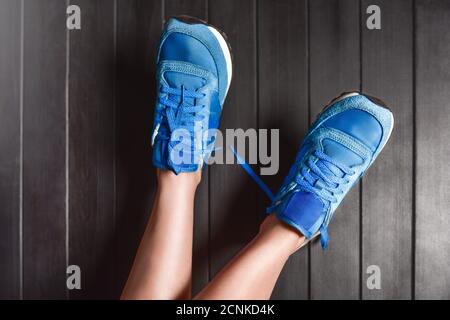 Close up fashion image of woman's feet, wearing sport sneakers on wooden background. lazy woman concept . rest concept. Untied s Stock Photo