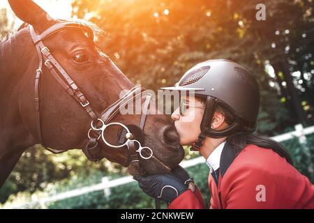 A young girl jockey talking to her horse. She loves the animals and joyfully spends her time in their environment. Stock Photo