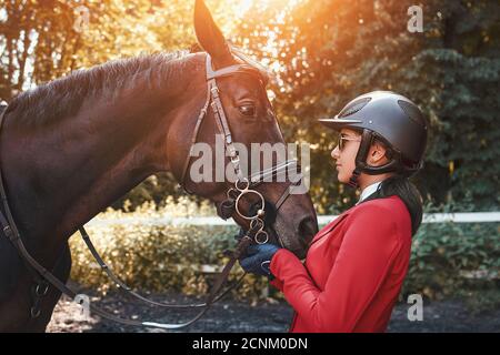 A young girl jockey talking to her horse. She loves the animals and joyfully spends her time in their environment. Stock Photo