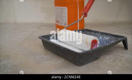 A worker pours a primer from an orange canister.. Worker pouring a primer in a paint tray Stock Photo