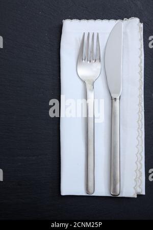 Table setting, business lunch. Fork knife and white linen napkin isolated on black background, vertical top view Stock Photo