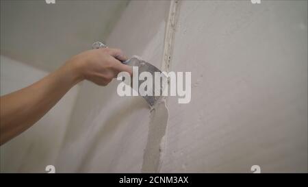Worker spreads mortar on the wall. Wall repair in a new apartment. Hand of worker with plaster and trowel to gypsum board Stock Photo