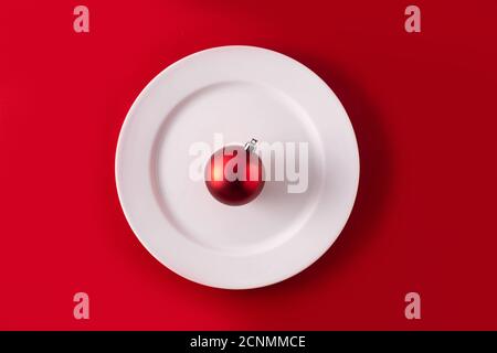 Red Christmas ball on white plate . Christmas dinner concept. Stock Photo