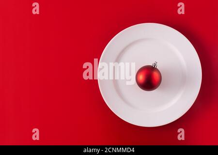 Red Christmas ball on white plate . Christmas dinner concept. Stock Photo