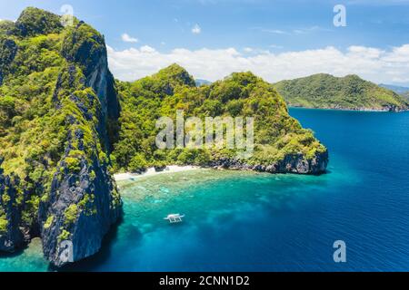 Aerial drone view of tropical beach with lonely boat on Entalula Island. Karst limestone formation mountain surrounded by blue ocean and beautiful cor Stock Photo