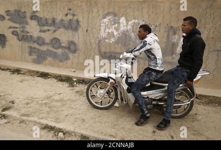 Unemployed men sit on motorcycle beside a graffiti which reads 'Marginalized youth' at the impoverished Zhor neighborhood of Kasserine, where young people have been demonstrating for jobs since last week, January 28, 2016. REUTERS/Zohra Bensemra