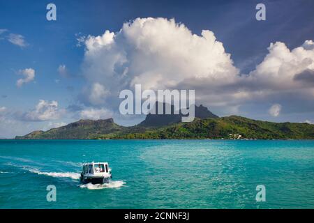 Seascape view with small boat in foreground, of Bora Bora Island with Mount Otemanu in centre with blue sky and white cloud, French Polynesia Stock Photo