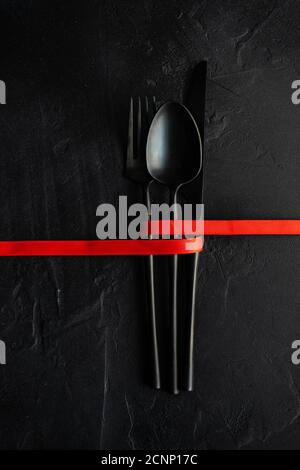 Red ribbon tied around cutlery on a black background Stock Photo