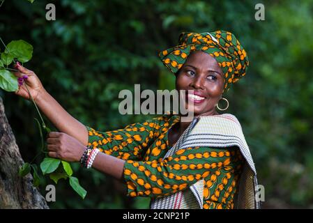 smiling african woman in traditional clothes taking care of plants during the walk in the nature Stock Photo