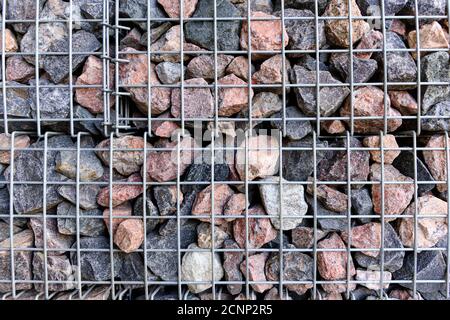 The wall of large granite stones in the grid. The texture of the stone wall is covered with a metal mesh. Stock Photo