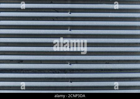 The old gray corrugated metal wall made of sheets with bolts. The corrugated metal texture. Stock Photo