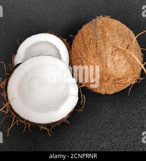 A whole and a half coconut. Vegetarian food. Coconut on a black background. Stock Photo