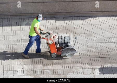 Construction worker cutting paving stone floor with diamond saw blade machine on a sidewalk Stock Photo
