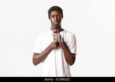 Portrait of young african-american guy performing song, holding microphone and singing karaoke, white background Stock Photo