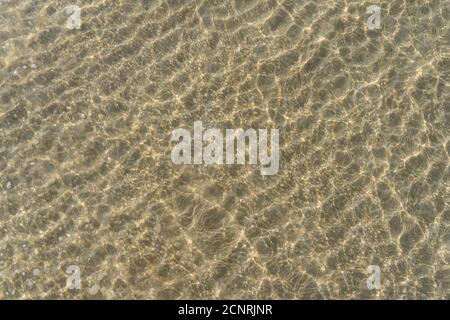 Aerial top view of clear water and patterned sand as the tide comes in at the beach. Stock Photo