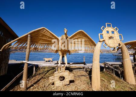 A condor and representation of the sun god made of reeds on the Uros Islands, Lake Titicaca, Peru. A dog walks in the background Stock Photo