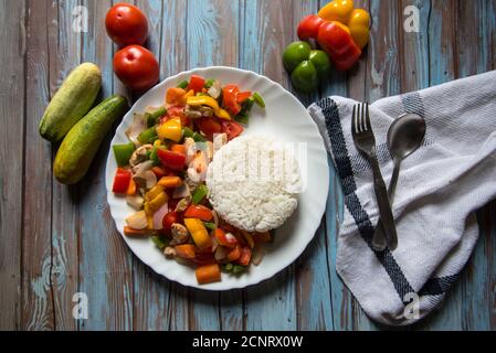 Steamed rice along with chicken and vegetables saute in a white plate with ingredients on a background