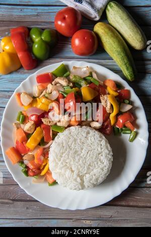 Top view of steamed rice along with chicken and vegetables saute in a white plate with ingredients on a background Stock Photo