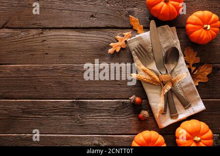 Autumn harvest or thanksgiving table scene with silverware, napkin, leaves and pumpkin border against a rustic dark wood background Stock Photo