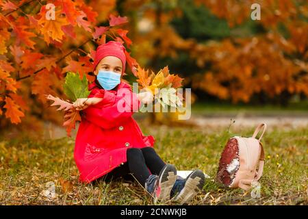 Little girl wearing medical face mask prevent pollution on fallen leaves at park. Stock Photo